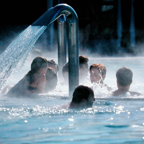 Menschen, die sich in einem Wasserbecken um einen Wasserstrahl gruppieren. Die Wasseroberfläche dampft.