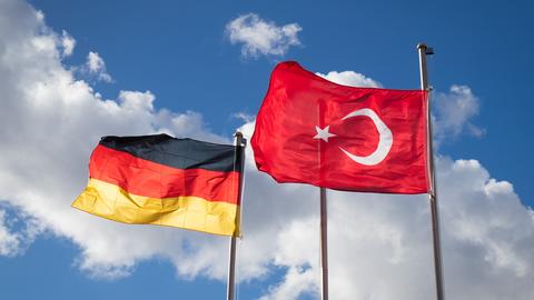 Eine deutsche und eine türkische Fahne wehen vor blauem Himmel