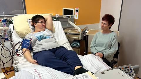 Saskia Wollenhaupt liegt auf einem Krankenhausbett und ist an Dialyse angeschlossen, ihre Mutter Sandra sitzt neben dem Bett. 