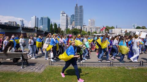 Mit ukrainischen Fahnen und Plakaten sind die hauptsächlich weiblichen Teilnehmerinnen bei einer Demonstration unter dem Motto "Mütter gegen den Krieg in der Ukraine und in Europa" am Frankfurter Mainufer unterwegs.