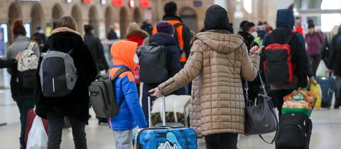 Frauen und Kinder gehen mit Koffern durch eine Bahnhofshalle