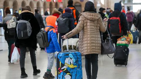 Frauen und Kinder gehen mit Koffern durch eine Bahnhofshalle