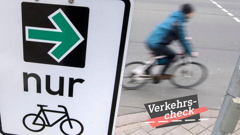 Rechts im Bild ein Radfahrer, leicht unscharf, weil er in Bewegung ist. Links davon ein Schild mit einem grünen Pfeil nach rechts, dem Wort "nur" und einem Fahradicon. Alles aus der näheren Vogelperspektive fotografiert. Auf dem Bild rechts unten eine kleine Grafik mit dem Wort "Verkehrs-Check".