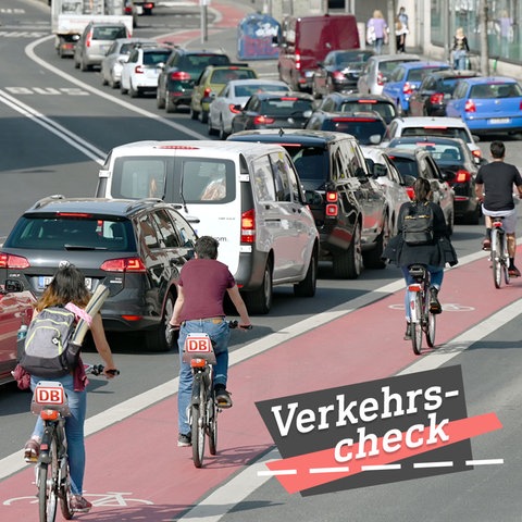 Blick eine große Straße entlang, wobei mehrere Radfahrer auf einem roten Fahradweg rechts neben Autos, die im Stau stehen., fahren. Alle sind von hinten und in Reihung zu sehen. Auf dem Bild rechts unten eine kleine Grafik mit dem Wort "Verkehrs-Check".