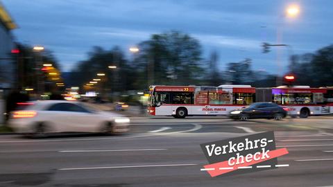 Eine große Straße in der Dunkelheit. Fahrende Autos ziehen durch ihre Bewegung bunte unscharfe Spuren. In der Mitte des Bildes ein ÖPNV-Bus, auch fahrend, aber schärfer. Auf dem Bild rechts unten eine kleine Grafik mit dem Wort "Verkehrs-Check".