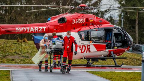 Ein Rettungshubschrauber, davor Rettungskräfte, die einen beatmeten Patienten auf einer Trage transportieren.