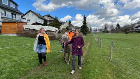 Ein Junge reitet ein Pony und wird von einer Frau geführt, eine andere Frau läuft vorne weg.