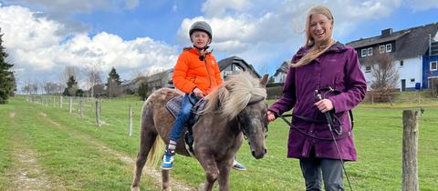 Ein Junge reitet ein Pony und wird von einer Frau geführt.