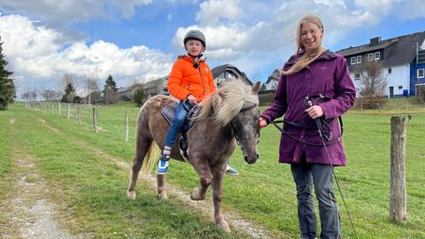 Ein Junge reitet ein Pony und wird von einer Frau geführt.