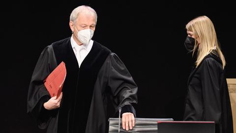 Der Richter mit einer roten Akte in der Hand wie er an einem der provisorisch eingerichteten Tische Platz nimmt.