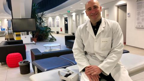 Ein Mann im Arztkittel auf einer Liege, daneben liegt eine VR-Brille