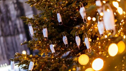 Mehrere Einwegmasken hängen an einem beleuchteten Weihnachtsbaum