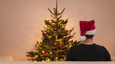 Mann mit Nikolausmütze sitzt alleine vor einem Weihnachtsbaum