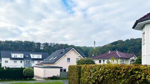 Fotografischer Blick in eine Einfamilienhaussiedlung. Darin bzw. dahinter in einer Grünfläche ein kleiner Schornstein.