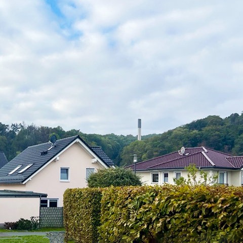 Fotografischer Blick in eine Einfamilienhaussiedlung. Darin bzw. dahinter in einer Grünfläche ein kleiner Schornstein.