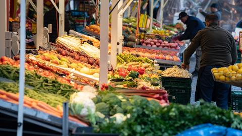 Der Wochenmarkt an der Berger Straße: Ein Stand mit viel Obst und Gemüse ist zu sehen, rechts stehen Männer, die weiteres Gemüse einsortieren.