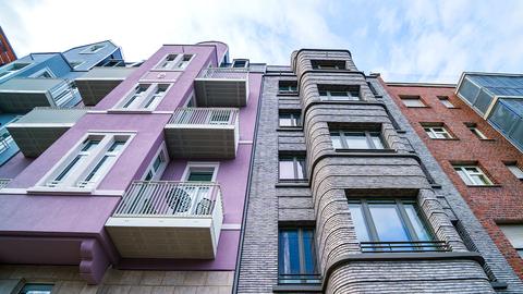Foto: Farbige Stadthäuser mit Balkonen von außen, aus der Perspektive eines Fußgängers, der die Fassade nach oben hin anguckt.