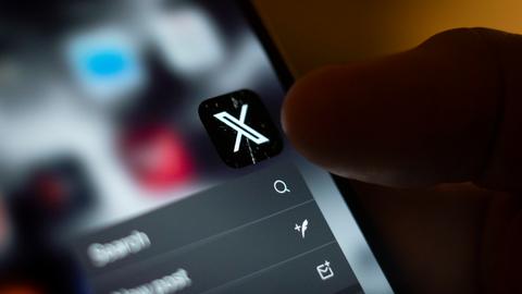 Jemand tippt mit dem Finger die App "X" auf dem Smartphone an. 