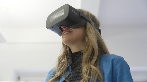 Eine junge Frau mit langen dunkelblonden Haaren trägt eine schwarze VR-Brille.