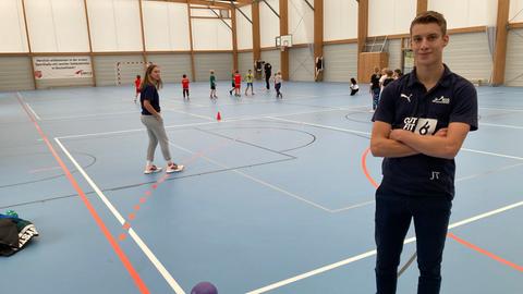 Jonas Trauth steht in der Handballhalle des TuS Griesheim, hinter ihm die Kinder, die er trianiert.