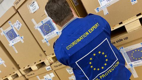 Mann mit EU-Logo auf Weste von hinten vor Kisten