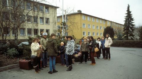 Lächelnde Menschengruppe in Winterkleidung vor gelben Mehrfamilienhäusern.