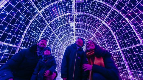 Eine Familie mit zwei Kindern betrachtet einen blau beleuchteten Lichterbogen.