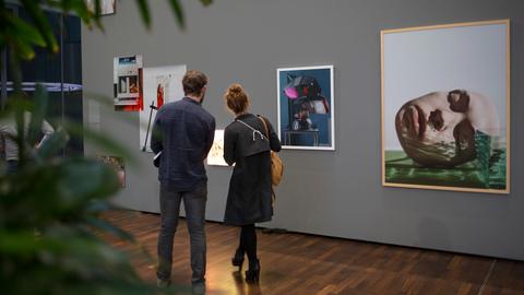 Ein Mann und eine Frau stehen vor einer Wand, an der verschiedene Fotografien hängen