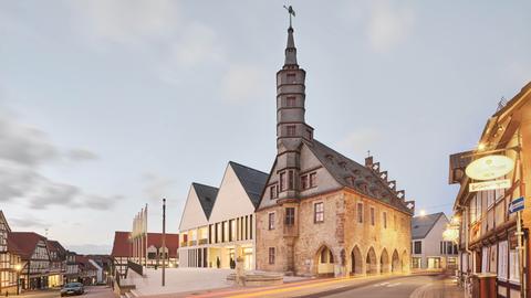 Historisches Rathaus mit spitzem Turm, daneben ein Neubau mit spitzen Giebeln.
