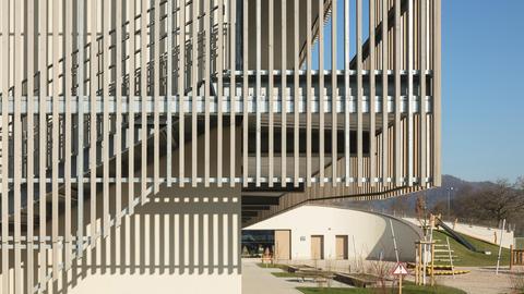 Gebäude mit einer Fassade aus Holzstäben, im Hintergrund ein Spielplatz