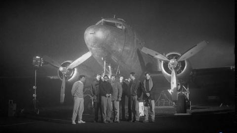 Die Schwarz-Weiß-Aufnahme zeigt acht Personen, die vor einer Propellermaschine stehen.