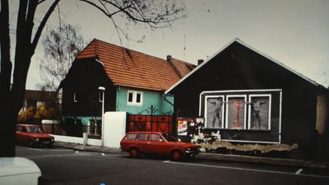Ein rotes Auto steht vor einem Haus, auf dem ein Wandbild angebracht wurde.