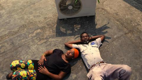 Filmstill: Zwei Menschen liegen vor einem Ventilator am Boden