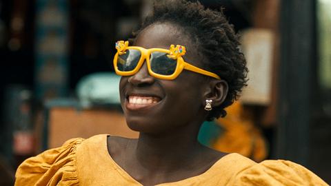 Ein dunkelkhäutiges Mädchen mit einer knallgelben Sonnenbrille lacht breit
