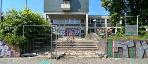 Auf dem Foto ist das alte Versorgungsamt in der Frankfurter Straße in Kassel zu sehen. Vor dem grauen Gebäude aus den 1970er Jahren haben die Architects 4 Future mit grellgrüner Farbe das #ichbinnochgut-Aktionssymbol gauf den Asphalt gesprüht.