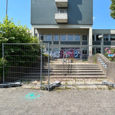 Auf dem Foto ist das alte Versorgungsamt in der Frankfurter Straße in Kassel zu sehen. Vor dem grauen Gebäude aus den 1970er Jahren haben die Architects 4 Future mit grellgrüner Farbe das #ichbinnochgut-Aktionssymbol gauf den Asphalt gesprüht.