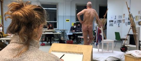 Aktmodell Stefan steht in der Mitte des Raumes und wird von den Teilnehmenden gezeichnet.