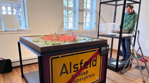 Ausstellung zum Stadtjubiläum in Alsfeld - Ansicht von der Schau - ein Stadtmodell steht auf einem Gestell an dessen Vorderfront ein Alsfeld-Verkehrsschild hängt. 