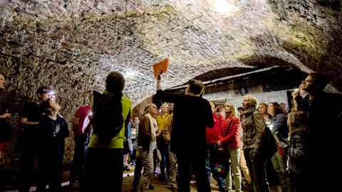 Menschen stehen in einem dunklen historischen Gewölbe und schauen mit Taschenlampen die Decke an