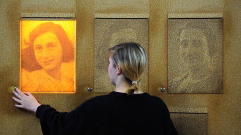 Eine Frau bedient der Bildungsstätte Anne Frank eine Lampe hinter einem Portrait von Anne Frank.