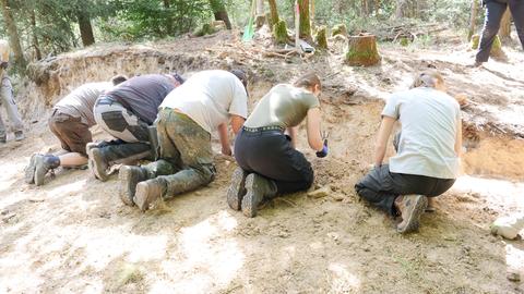 Fünf Menschen knieen vor einem Erdhügel und graben in der Erde.