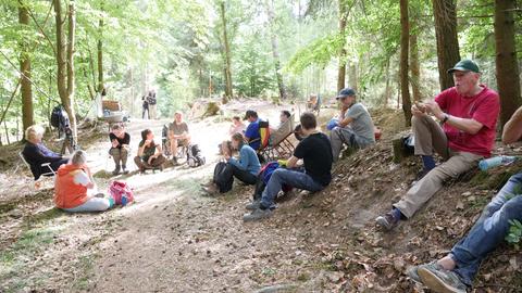Eine Gruppe von Leuten macht auf dem Waldboden sitzend Frühstückspause