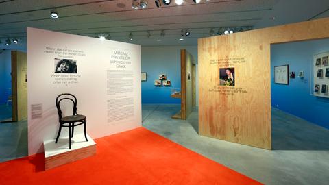 Ausstellungsansicht mit Stellwänden, Fotos, Vitrinen vor blauen Wänden und einem roten Boden