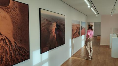 Eine Frau mit pinkfarbenen Oberteil steht vor einer Wand mit Fotos