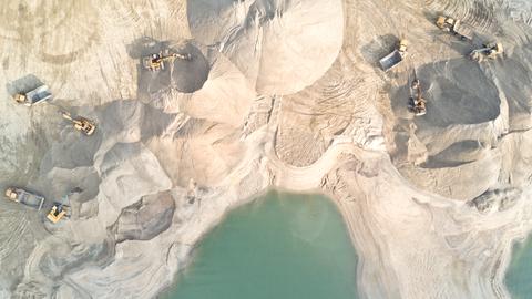 Blick aus der Vogelperspektive auf mehrere Bagger, die am Strand Sand wegbaggern