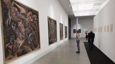 Ausstellungshalle mit braun-rötlichen Bildern von nackten Menschen.