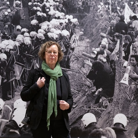 Eine ältere Frau mit grünem Schal steht vor einem großen schwarz-weiß-Foto
