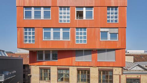 Aufbau mit orangefarbener Fassade auf einem Backstein-Gebäude