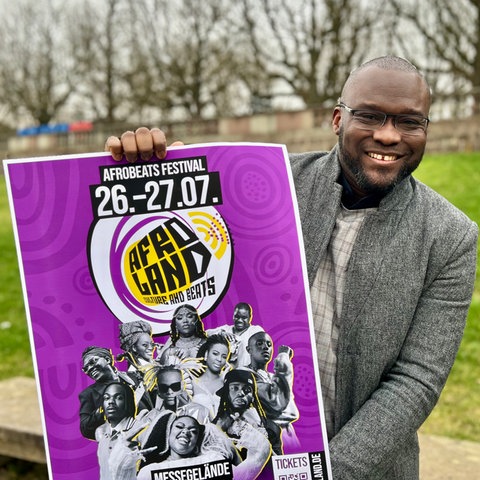 Belmond Gad, Mitorganisator des Afroland-Festivals in Fulda, zeigt ein Plakat der zweitägigen Musik-Veranstaltung
