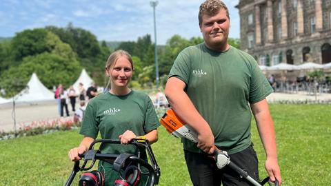 Eine junge Fraau und ein junger Mann in grünen T-Shirts und mit Gartengerät